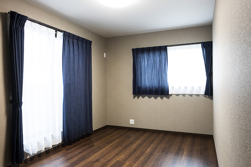 旦那様のお部屋はブラウンのクロスとブルーのカーテンで、主寝室とは少し違った落ち着いた雰囲気にコーディネートされました。（床：マイフロア　ウォールナット柄アンバー）