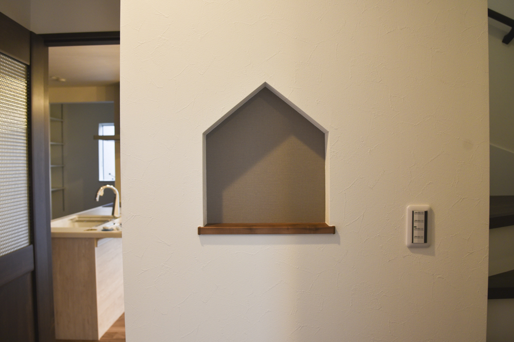 玄関のお家型ニッチ（下枠：NODA アートクチュール アップル柄モカ色／背面クロス：シンコール SLP-834）