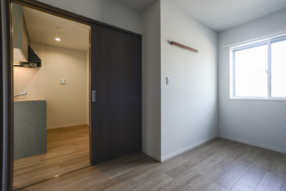 洋室:キッチンを向いたアングル(壁付ハンガーラック:住友クレスト ナットトイレカウンター柄)※101号室